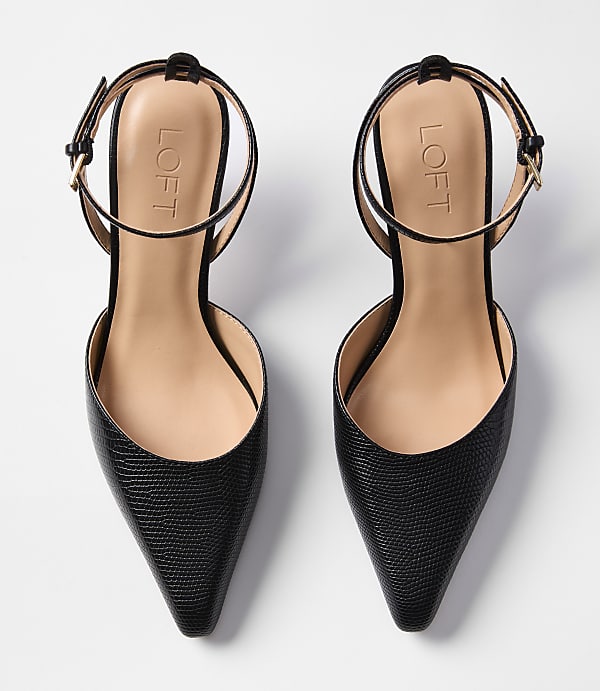 A pair of black, pointed-toe slingback heels with ankle straps rests on a plain white background.