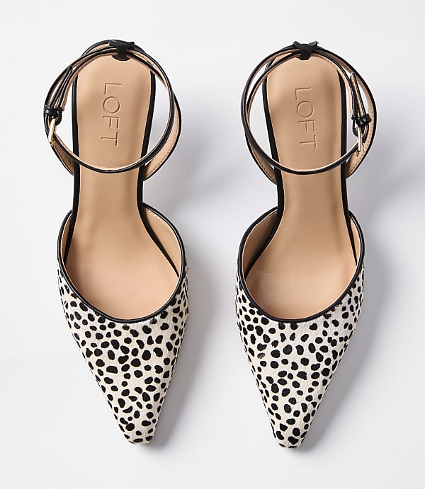 A pair of dalmatian-print pointed-toe flats with ankle straps rests on a plain white background.