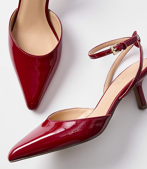 A pair of shiny red patent leather slingback heels with pointed toes and ankle straps are displayed against a plain white background.