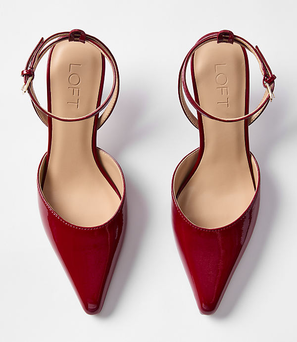 A pair of shiny red pointed-toe flats with ankle straps rests on a plain white background.