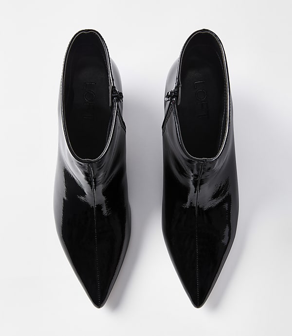 A pair of glossy black pointed-toe ankle boots with zippers are laid out on a plain white background.