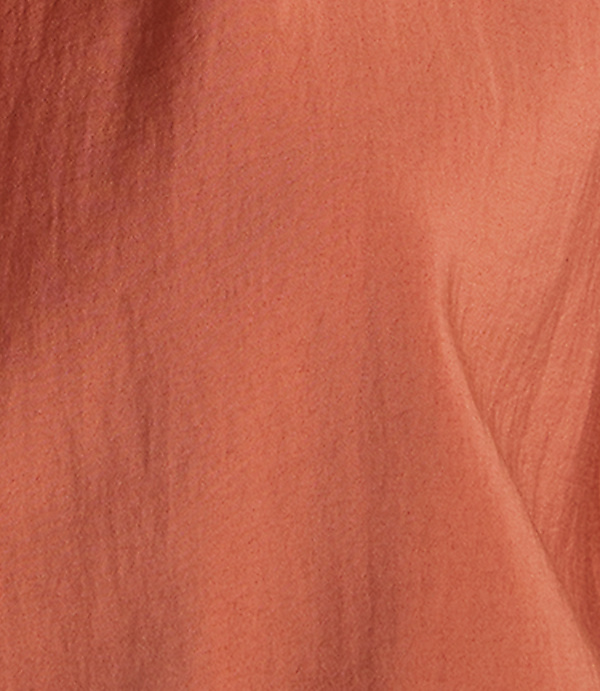 A close-up of a textured, coral-colored fabric fills the frame, with subtle folds and shadows creating depth.