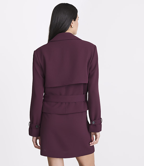 A woman in a burgundy jacket and skirt stands against a plain white background.