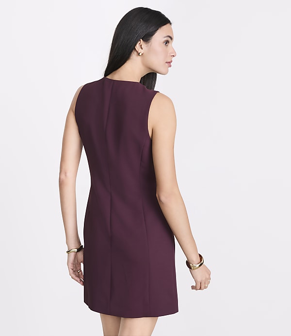 A woman in a burgundy sleeveless dress stands against a plain white background.