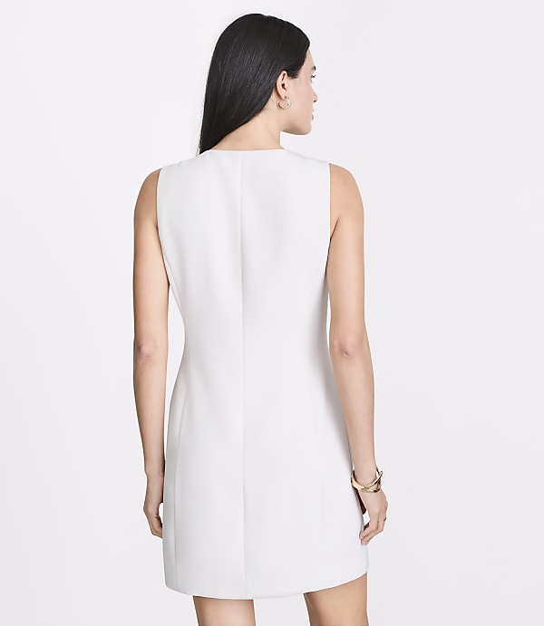 A woman in a white sleeveless dress stands against a plain white background.