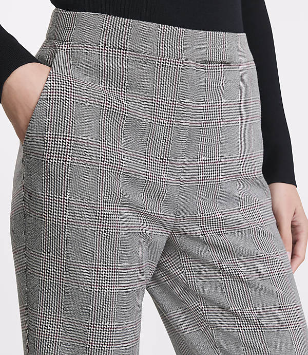 A person's hands are in the pockets of grey plaid pants, with a black top visible in the background.