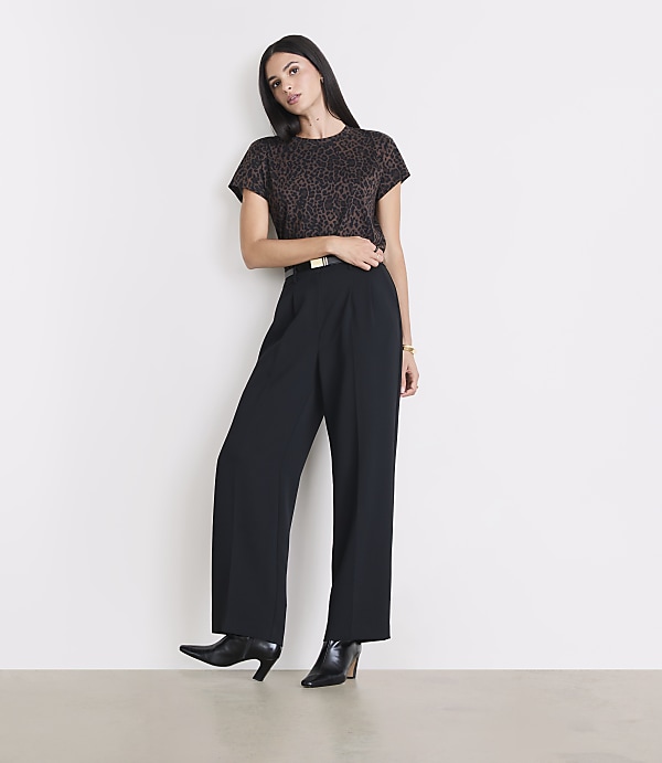 A woman in a leopard print top and black wide-leg pants stands against a plain white background.