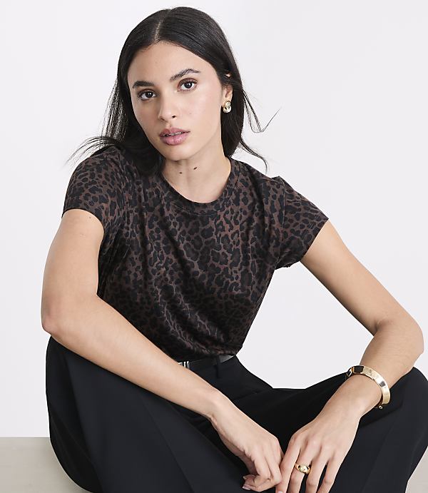 A woman in a leopard print t-shirt and black pants sits against a plain white background.