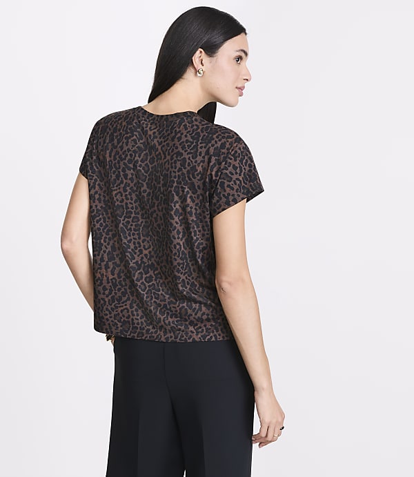 A woman in a leopard print top and black pants stands against a plain white background.
