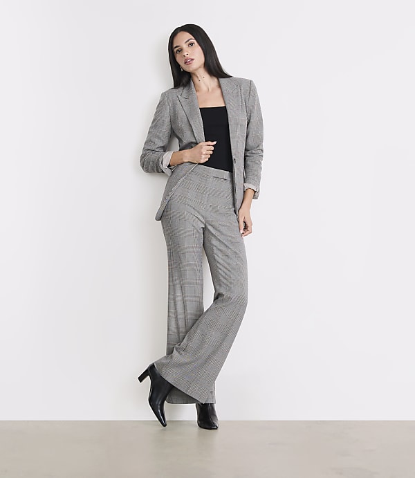 A woman in a plaid suit stands against a white wall with a light-colored floor in the foreground.