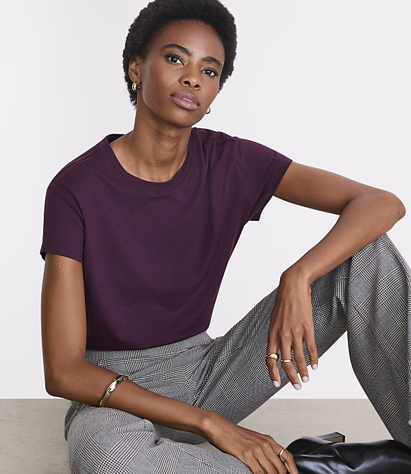 A woman in a plum t-shirt and checkered pants sits against a plain white background.