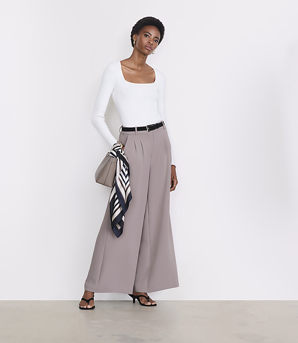 A woman in a white top and wide-leg pants stands against a plain white background.