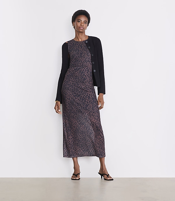 A woman in a leopard print dress and black cardigan stands against a plain white background.