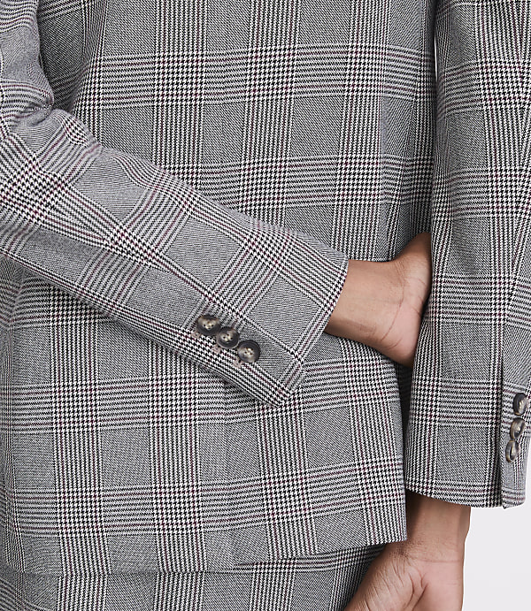 A person's hand is tucked into the pocket of a grey plaid suit jacket, with the background also showing the same suit fabric.