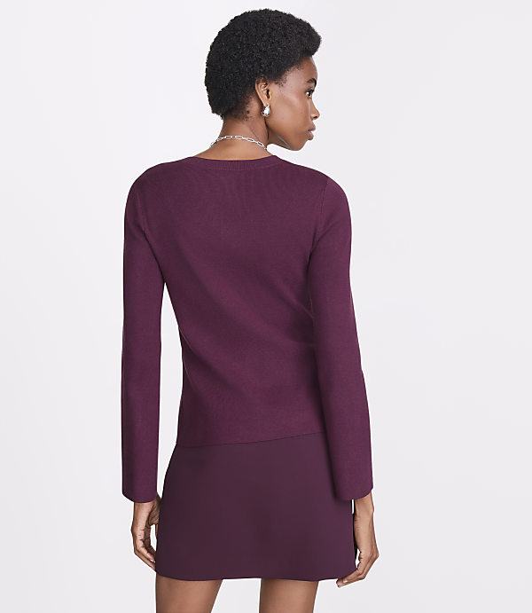 A woman in a burgundy sweater and skirt stands against a plain white background.