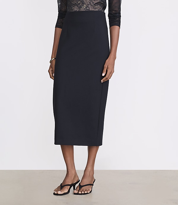 A woman in a black pencil skirt and lace top stands on a light gray floor against a white background.