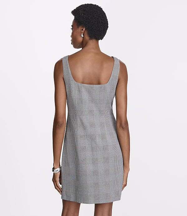 A woman in a plaid dress stands against a plain white background.