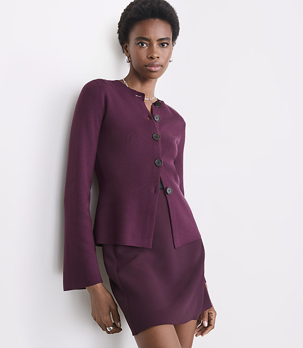A woman in a burgundy cardigan and skirt stands against a plain white wall.