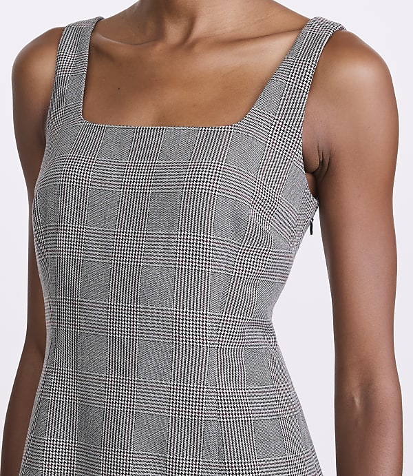 A woman in a plaid dress with a square neckline stands against a plain background.