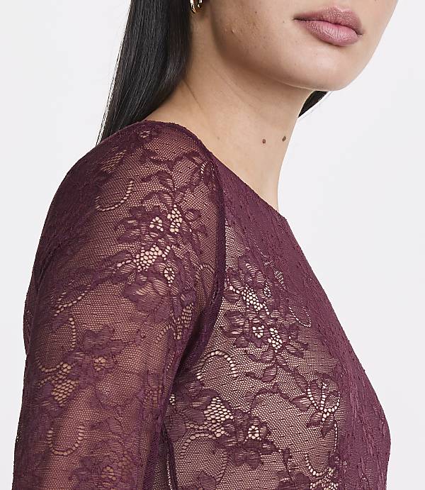 A woman in a burgundy lace top is shown from the chest up against a plain white background.