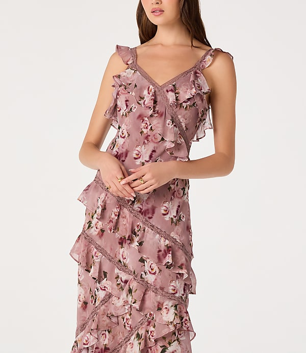 A woman in a floral ruffled dress stands against a plain white background.