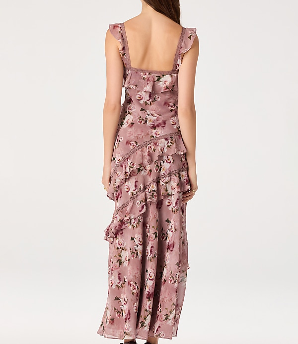 A woman in a ruffled, floral-print dress stands against a plain white background.