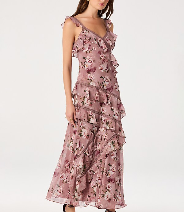 A woman in a ruffled, floral maxi dress stands against a plain white background.