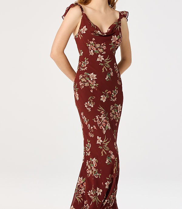 A woman in a floral print dress stands against a plain white background.