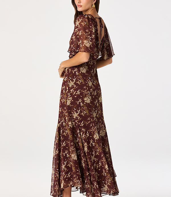 A woman in a floral print dress stands against a plain white background.