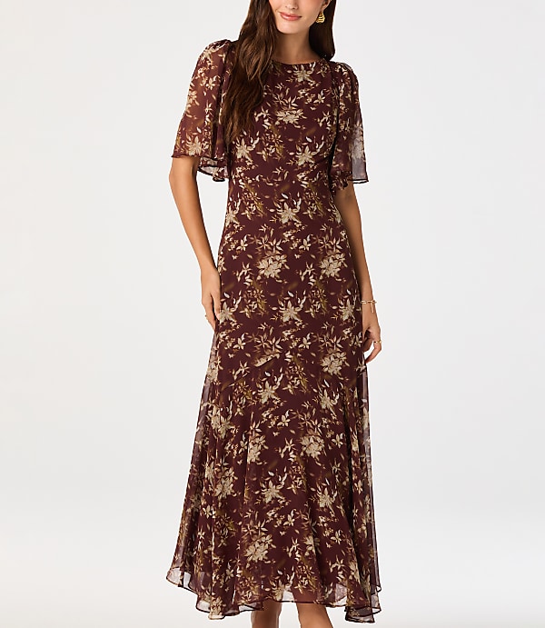 A woman in a floral dress stands against a plain white background.