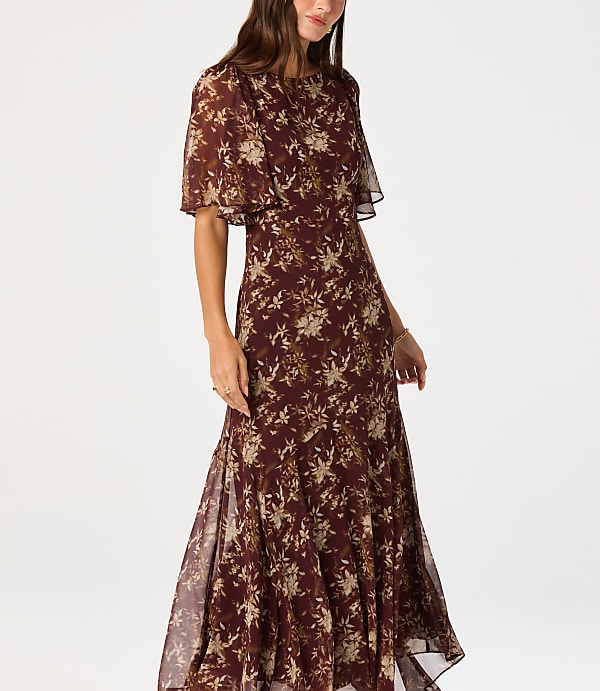 A woman in a floral dress stands against a plain white background.