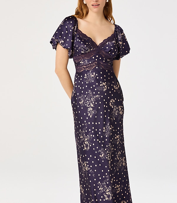 A woman in a dark blue polka dot dress with lace detailing stands against a plain white background.