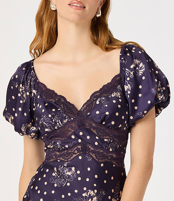 A woman in a dark blue polka dot dress with lace trim is shown against a plain white background.
