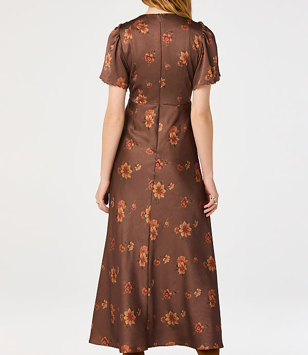 A woman in a brown floral dress stands against a plain white background.