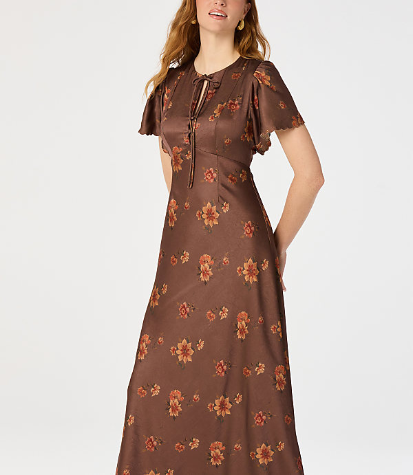 A woman in a brown floral dress stands against a plain white background.