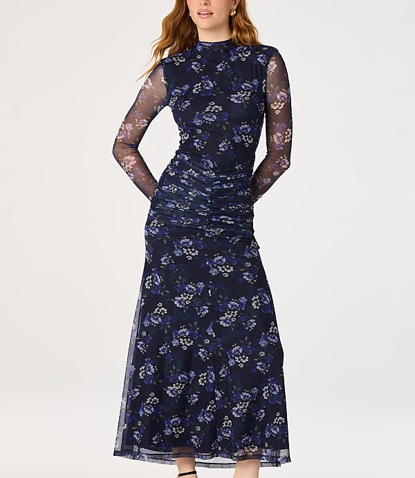 A woman in a dark floral mesh dress stands against a plain white background.