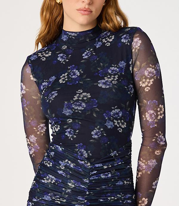 A woman in a dark blue floral mesh top with ruched detailing stands against a plain white background.
