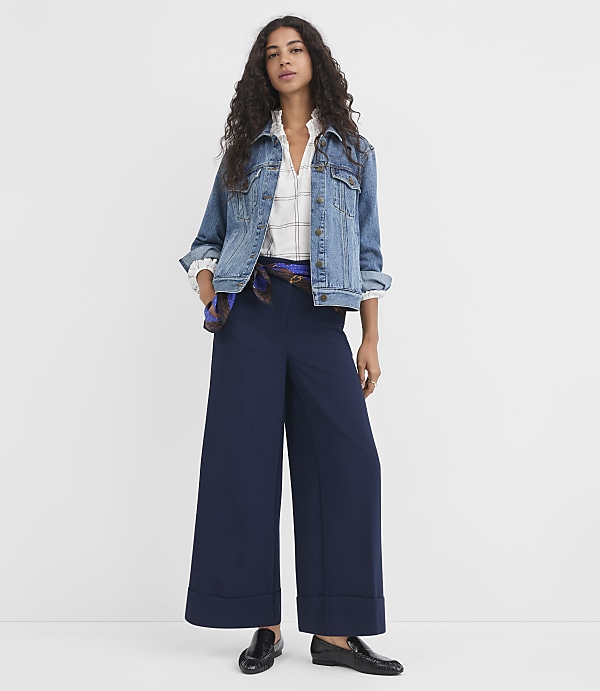 A woman in a denim jacket and wide-leg navy pants stands against a plain white background.