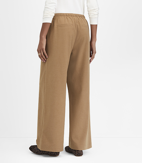 A person wearing tan wide-leg pants and leopard print shoes stands against a plain white background.