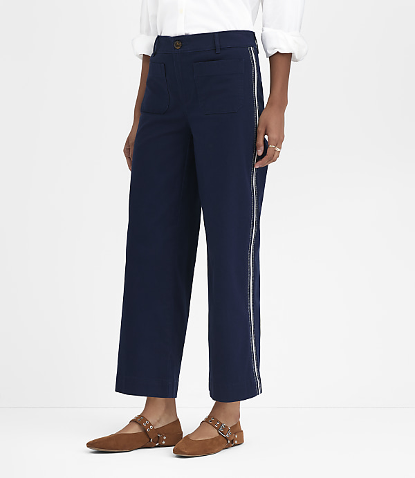 A person in navy blue cropped pants with white side stripes and brown flats stands against a plain white background.