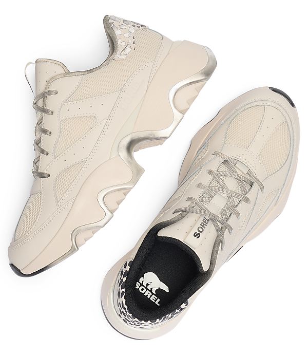 A pair of light beige Sorel sneakers with grey laces and a white sole are laid out on a white background, with a hint of leopard print visible on the heel of one shoe.