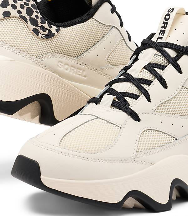 A pair of cream-colored Sorel sneakers with black laces and leopard print accents are displayed against a white background.