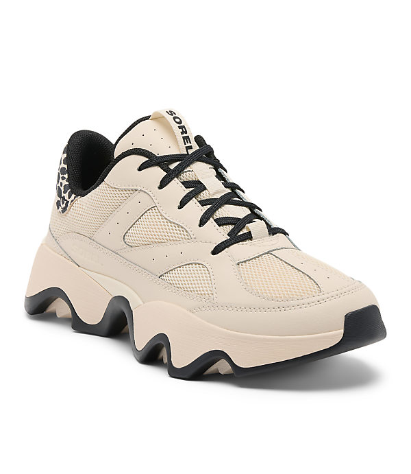 A light beige Sorel sneaker with black laces and leopard print accents sits on a white background.