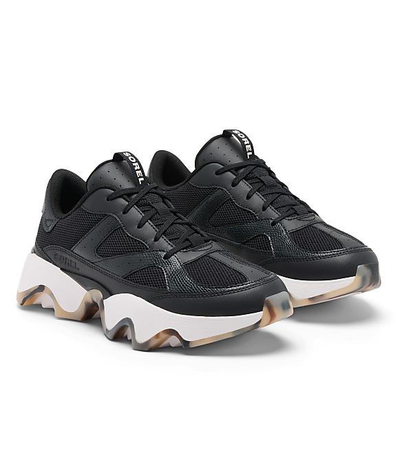 A pair of black Sorel sneakers with chunky white soles and translucent, patterned outsoles rest on a plain white background.