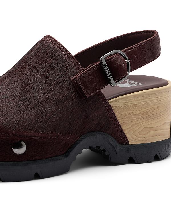 A close-up of a burgundy, furry clog with a wooden sole and a black rubber sole is set against a plain white background.