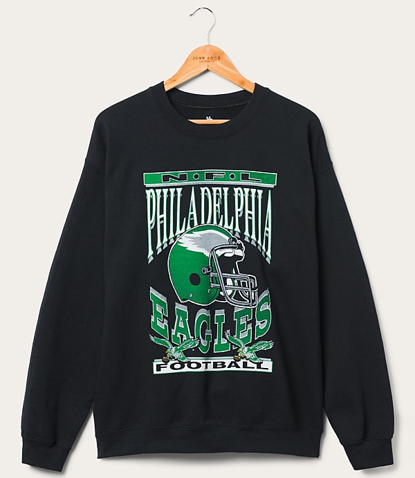 A black Philadelphia Eagles sweatshirt with a graphic of a helmet and eagles hangs on a wooden hanger against a plain white background.