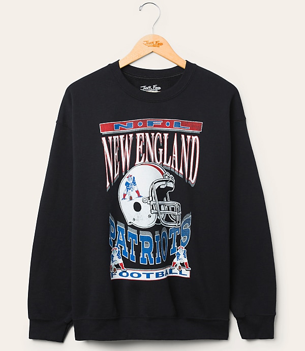 A black New England Patriots sweatshirt with a graphic of a helmet and team name hangs on a wooden hanger against a plain, light-colored background.