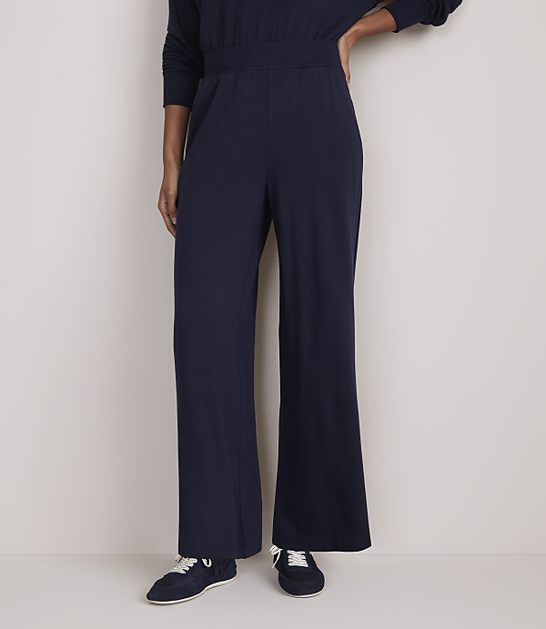 A person stands in navy blue wide-leg pants and sneakers against a plain, light-colored background.