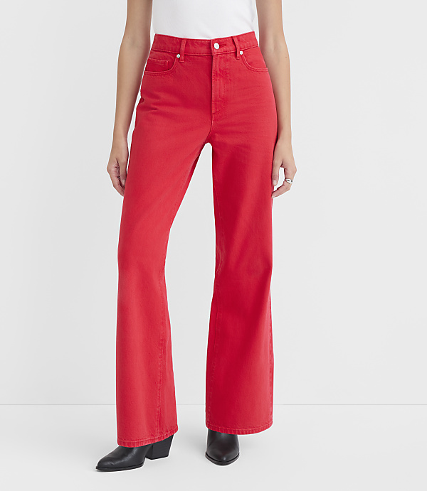 A person stands in the foreground wearing bright red flared jeans and black boots against a plain white background.