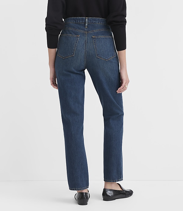 A person wearing dark wash jeans and black loafers stands against a plain white background.